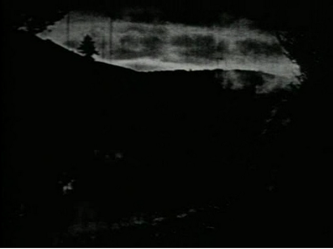 A dark, heavily distorted landscape with a tree line.